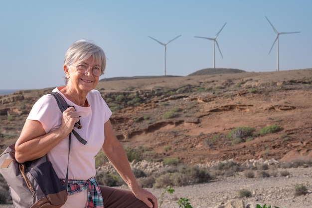 Parque eólico de energía alternativa en la montaña Mujer madura feliz senderismo en el campo de las turbinas eólicas