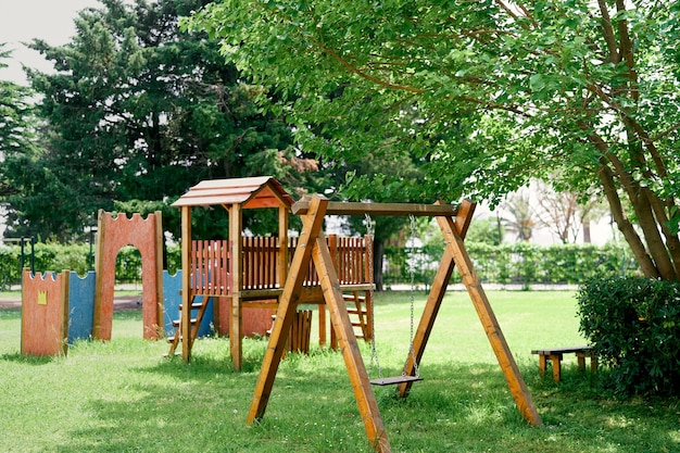 Parque infantil de madera con columpios en un césped verde entre los árboles