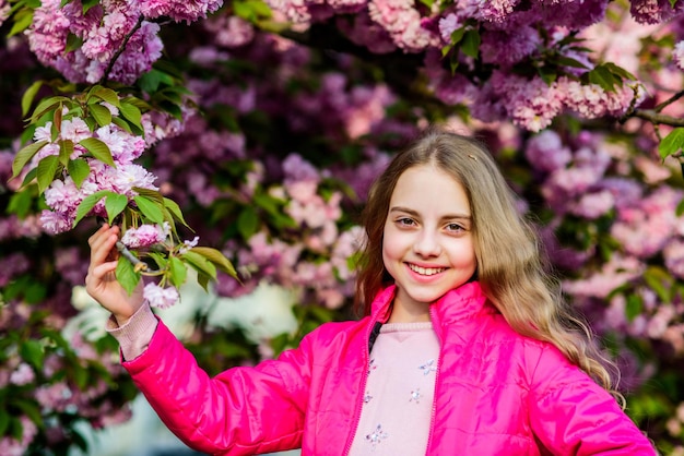 Parque y jardín. Niña pequeña en flor de primavera. Disfruta del olor de la tierna floración del día soleado. Concepto de flor de sakura. Preciosa belleza de flores. Fondo de flor de cerezo de niña. Árbol de sakura floreciendo.