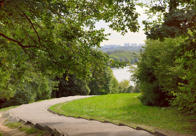 Parque kolomenskoe camino pavimentado para peatones que baja hasta el río casas en el horizonte