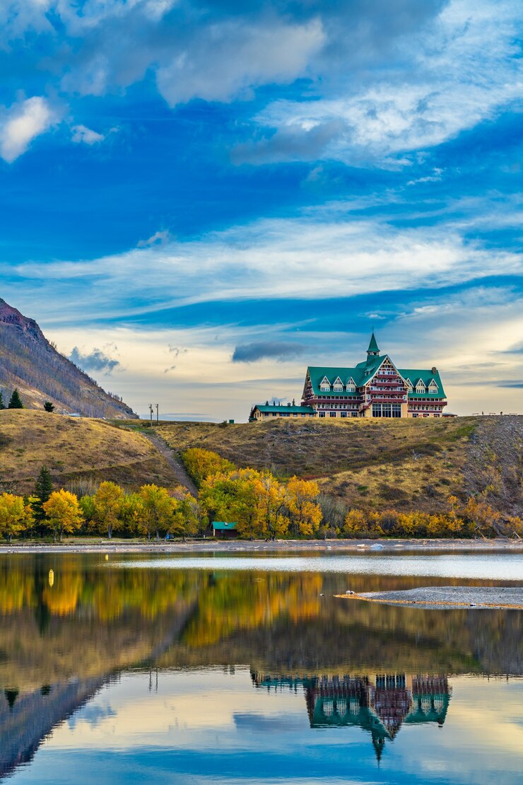 Parque Nacional Waterton Lakes a orillas del lago en la temporada de follaje de otoño por la mañana. Cielo azul, nubes de colores se reflejan en la superficie del lago como un espejo al amanecer. Paisaje de color de otoño. Sitios de interés en Alberta, Canadá