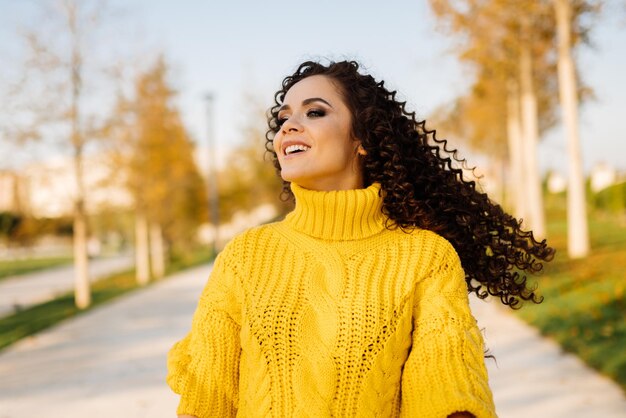 En el parque de otoño, una niña bellamente sonriente con un suéter brillante