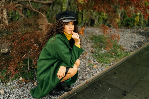 Foto en el parque en el remanso se sentó una chica con un abrigo verde y una gorra y mira cuidadosamente algo