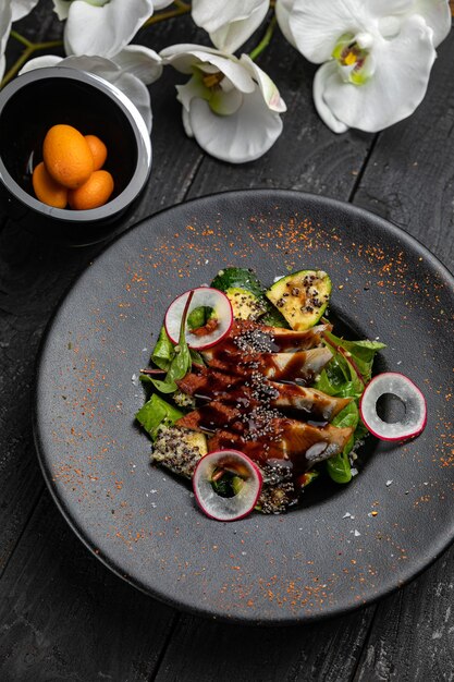 Parrilla de anguila con calabacín y ensalada en un plato oscuro