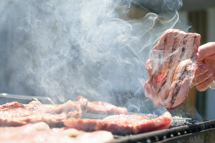 Una parrilla con carne y humo saliendo de ella.