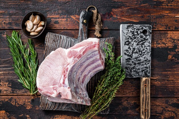 Foto parrilla cruda de chuletas de lomo de cerdo con costillas en una placa de carnicero con cuchillo de carnicero