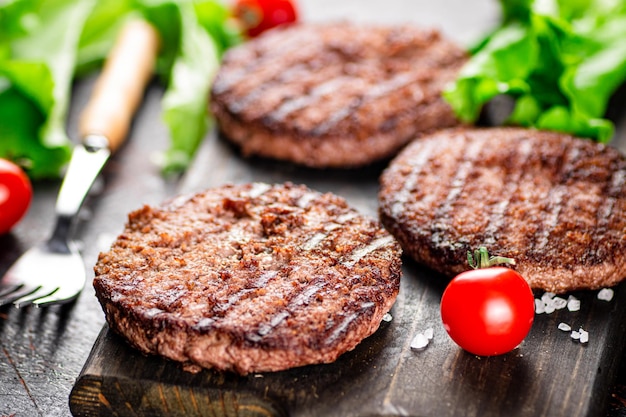 Parrilla de hamburguesas sobre una tabla para cortar con tomates y verduras