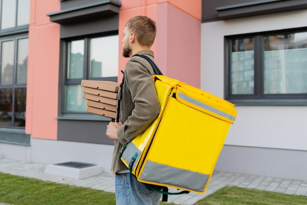 La parte de atrás de un mensajero masculino con una bolsa amarilla durante la entrega de pizza