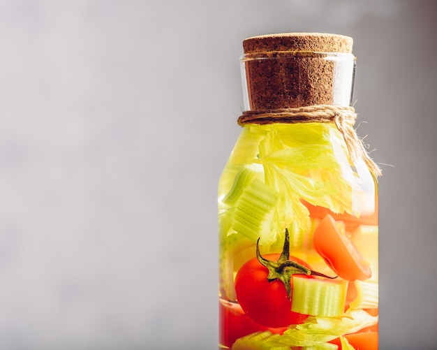 Parte de la botella con agua infundida con tomate cherry y tallos de apio. Copie el espacio a la izquierda.