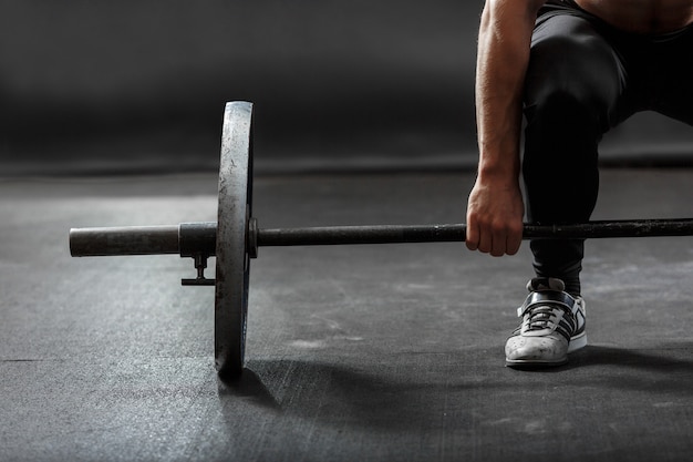 Una parte del brazo y la pierna del hombre, levantando la barra de gimnasia