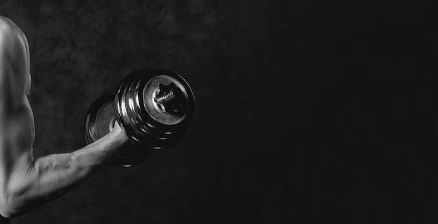 Parte del cuerpo del hombre con mancuernas de metal sobre fondo oscuro. Fotografía en blanco y negro