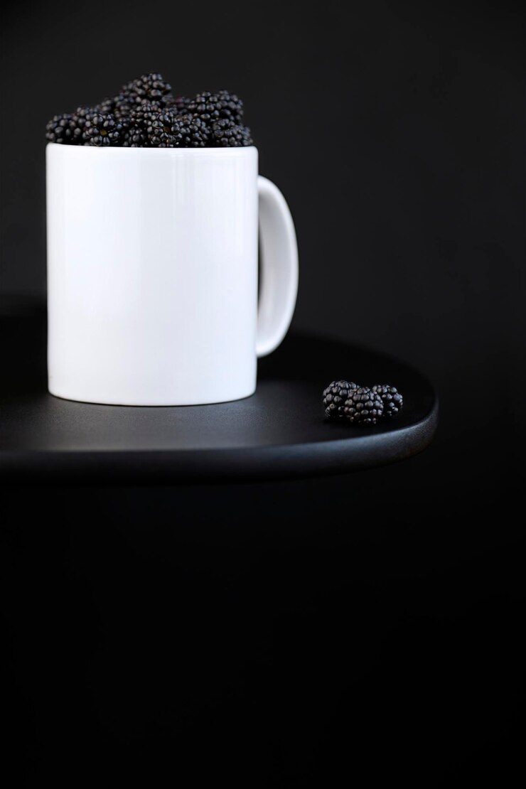 Foto parte de amoras dentro de uma caneca branca em fundo preto com espaço de cópia