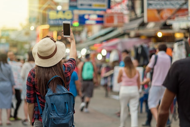 Parte de trás da jovem asiática viajando mulheres tirando foto em khaosan road andando pela rua à noite