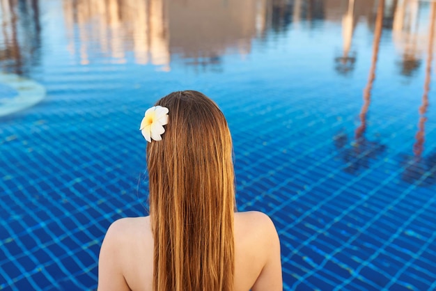 Parte de trás da mulher caucasiana com cabelo de tronco e flor nele sentado à beira da piscina