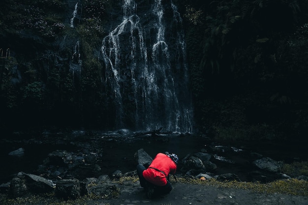 Parte de trás do fotógrafo em camiseta vermelha com fotografia de câmera moderna capturando a paisagem da cachoeira