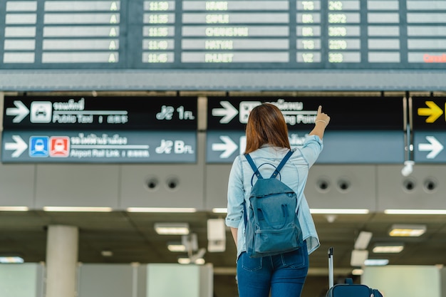 Parte de trás do viajante mulher asiática com pé de bagagem sobre a placa de vôo para check-in