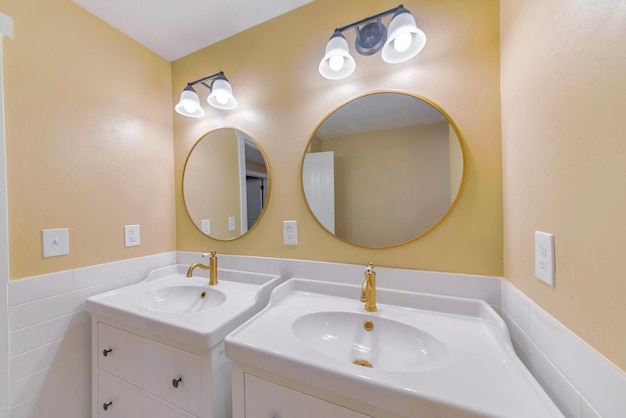 Parte de um projeto de banheiro com dois lavatórios e espelho redondo vintage na parede com a moldura dourada.