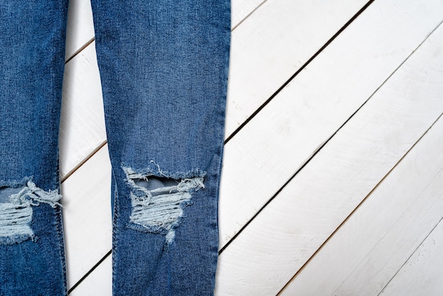 Parte de uma calça jeans esfarrapada azul em um fundo branco de madeira