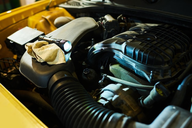 Parte do motor do carro elétrico com lanterna e espanador em capô aberto