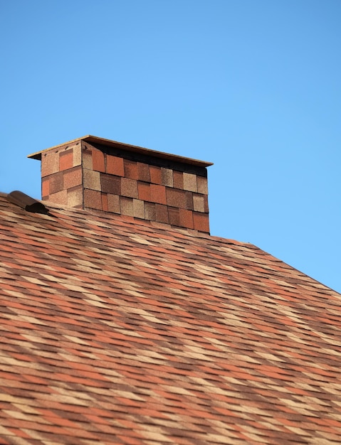 Parte do telhado castanho de uma casa coberta com telhas macias motley com curta grande chaminé