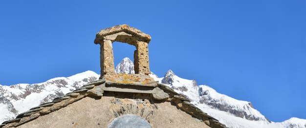 Parte do telhado da capela em frente a picos cobertos de neve sob o céu azul