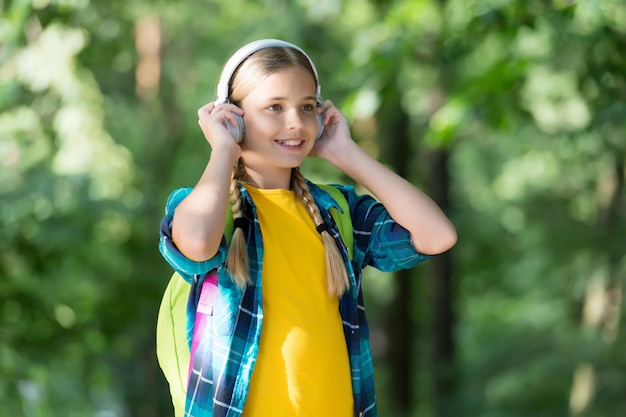 Parte essencial da vida moderna. A menina usa fones de ouvido naturais ao ar livre. Criança pequena ouvir música. Áudio Hi-Fi. Som digital. Tecnologia moderna. Férias de verão e viagens. Estilo de vida moderno.