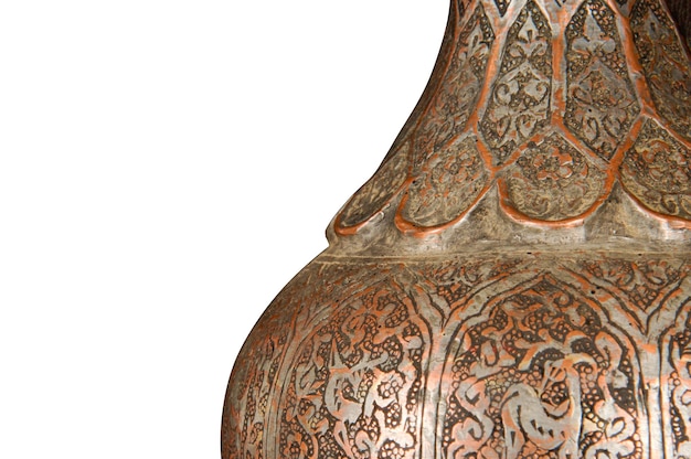 Una parte de una jarra de cobre antigua con persecución artística y grabado sobre un fondo blanco.