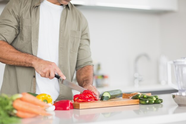 Parte média de um homem cortando vegetais na cozinha