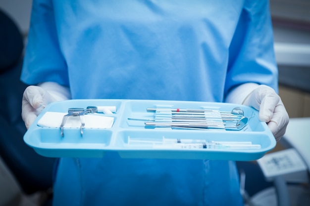 Foto parte média do dentista em esfrega azul segurando bandeja de ferramentas