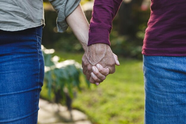 Parte media de una pareja caucásica de alto rango tomándose de la mano caminando en el jardín. estilo de vida de jubilación, pasar tiempo en casa.