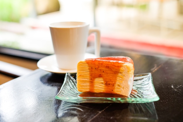 Parte del pastel de crepe cubierto con salsa de fresa sirve en un plato transparente y leche fresca y caliente en vaso