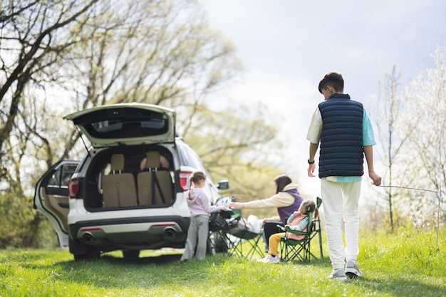 Parte posterior del muchacho adolescente contra la familia con el baúl abierto del coche en un picnic