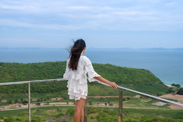 Parte posterior de la mujer asiática de pelo largo con viento de pie y mirando el panorama marino en el punto de vista de la terraza en la isla del pico de la montaña, Koh Larn high view point, Chonburi, Tailandia