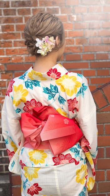 Foto parte posterior de la mujer japonesa en kimono con fondo de ladrillo rojo.