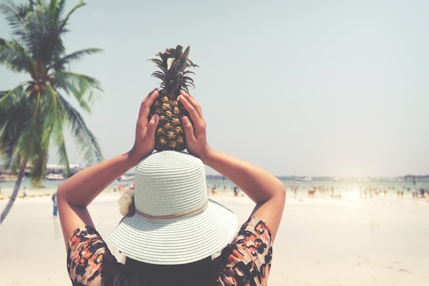 Parte posterior del retrato de la manera de la mujer hermosa con la piña fresca sostiene para arriba - vacaciones en la playa tropical en verano. estilos del color de la vendimia