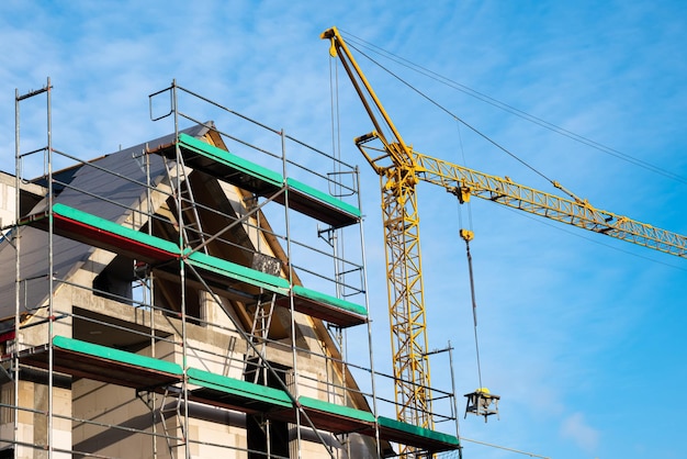 Parte superior de una casa sin terminar con andamios Grúa de construcción contra el cielo azul