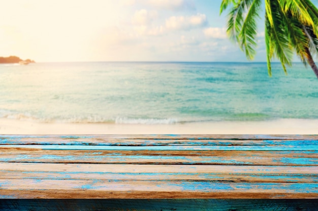 Parte superior de la mesa de madera en el mar borroso con el árbol de coco de fondo - vacío listo para su montaje de visualización de productos. Concepto de playa en verano. tono de color vintage