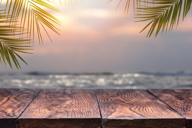 Parte superior de la mesa de madera en el mar borroso en la puesta de sol con fondo de árbol de coco. Vacío listo para el montaje de exhibición de su producto. Concepto de playa en verano.