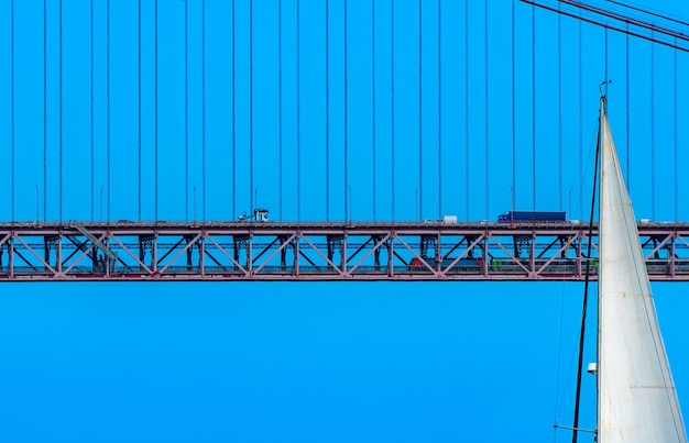 La parte superior de la vela blanca de un velero que navega frente al puente colgante de acero rojo 25 de Abril