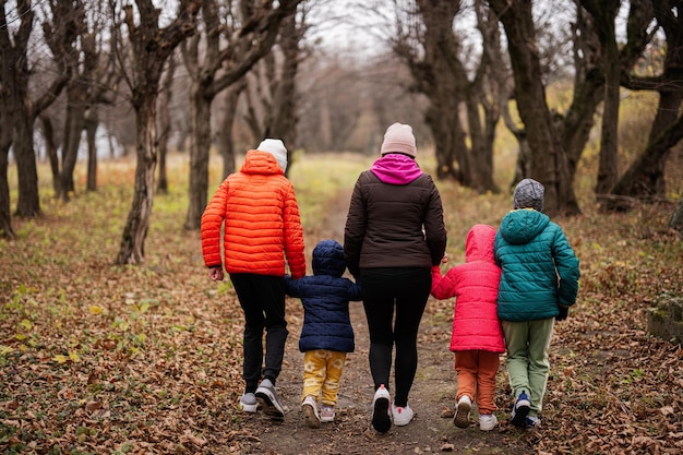 Parte traseira da mãe de mãos dadas com seus filhos andando na floresta de outono