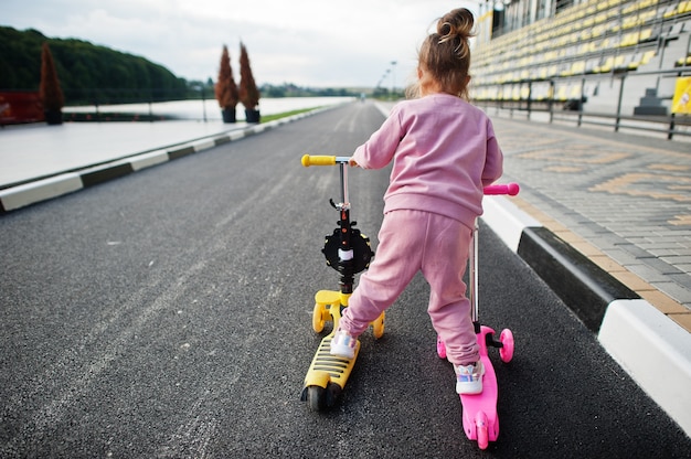 Parte traseira da menina em traje esporte rosa passeios de duas scooter.