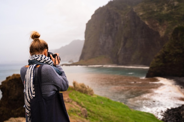 Parte traseira de um turista tirando fotos das falésias e do oceano