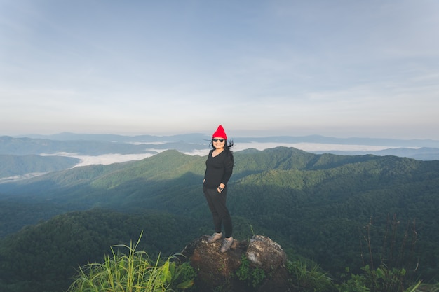 Foto parte traseira de uma mulher feliz no topo da montanha, olhando a vista com névoa e nuvens