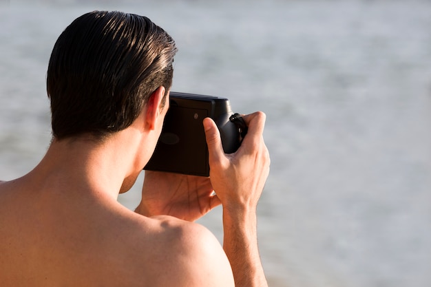 Parte traseira do homem tirando foto pela câmera instantânea na praia