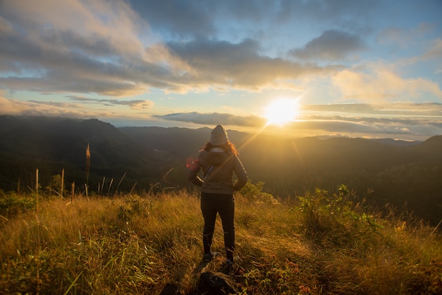 Parte traseira do suporte feliz da mulher na montanha superior que olha a vista com nascer do sol e névoa em Doi Langka Luang, província de Chiang Rai. foco suave.