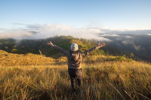 Parte traseira do suporte feliz da mulher na montanha superior que olha a vista com névoa e nuvem em Doi Langka Luang, província de Chiang Rai. foco suave.