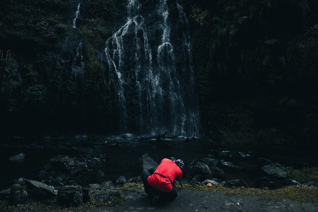 Parte trasera del fotógrafo en camiseta roja con fotografía de cámara moderna capturando paisaje de cascada