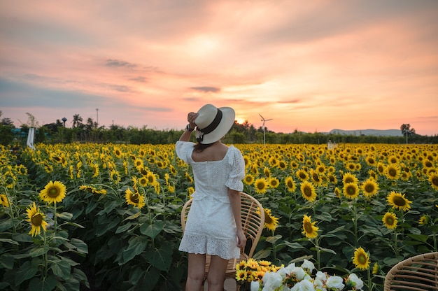 Parte trasera de la joven mujer asiática alegre de pie en el campo de girasol al atardecer