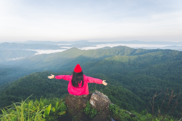 Foto parte trasera de una mujer joven sentada sobre una roca y ver la vista en la cima de la montaña