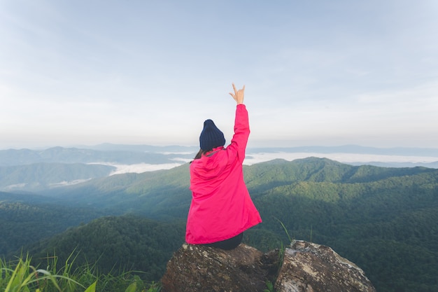 Foto parte trasera de una mujer joven sentada sobre una roca y ver la vista en la cima de la montaña